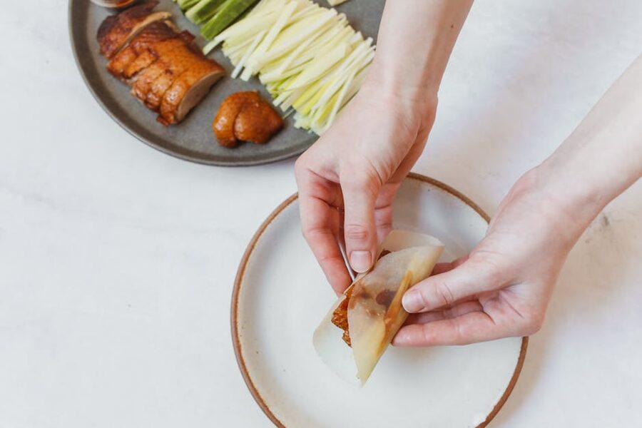 Hands wrapping Peking duck with cucumber and scallion in a pancake