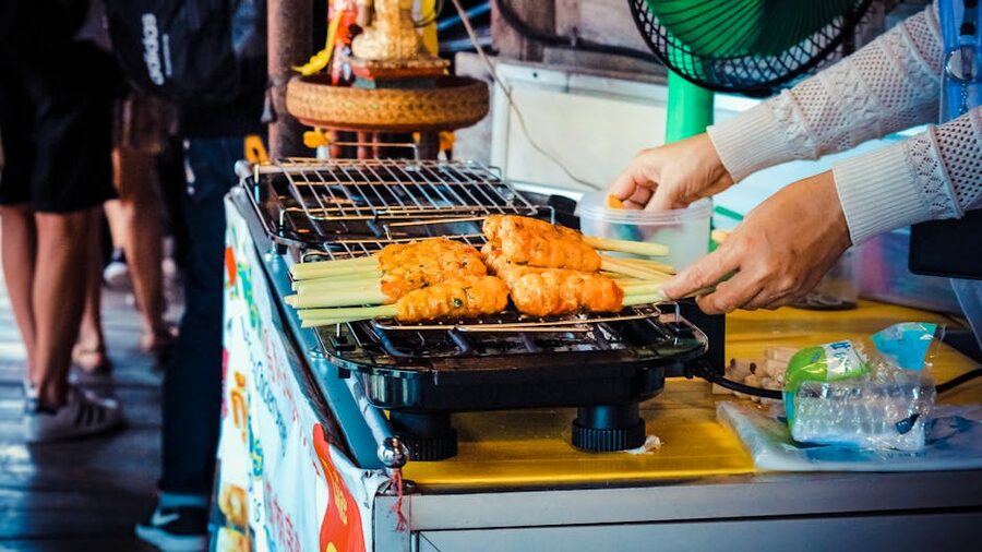Street vendor grilling satay skewers on electric grill
