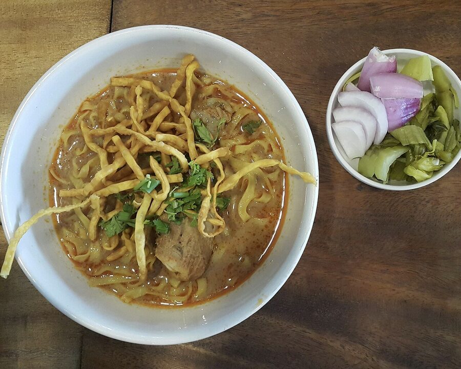 Bowl of Chiang Mai khao soi with pickled mustard greens on a saucer to the side