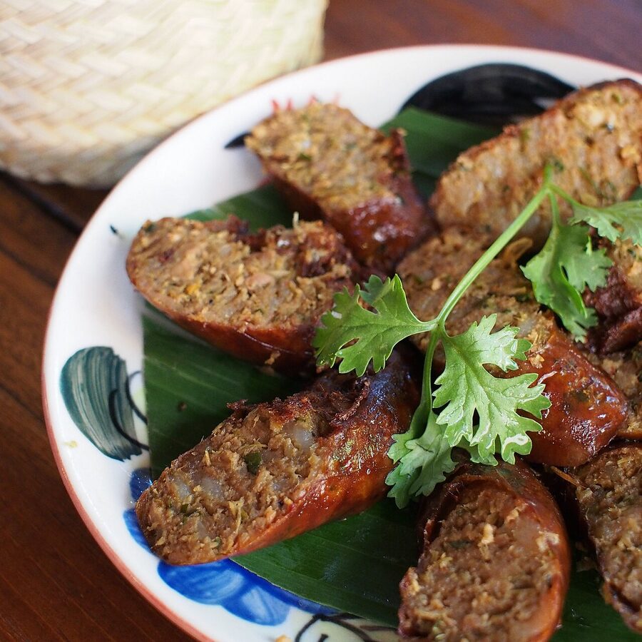 Coils of sai ua northern Thai pork sausage on a grill, with herbs visible