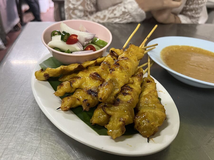 Thai pork satay skewers on a grill with peanut sauce nearby