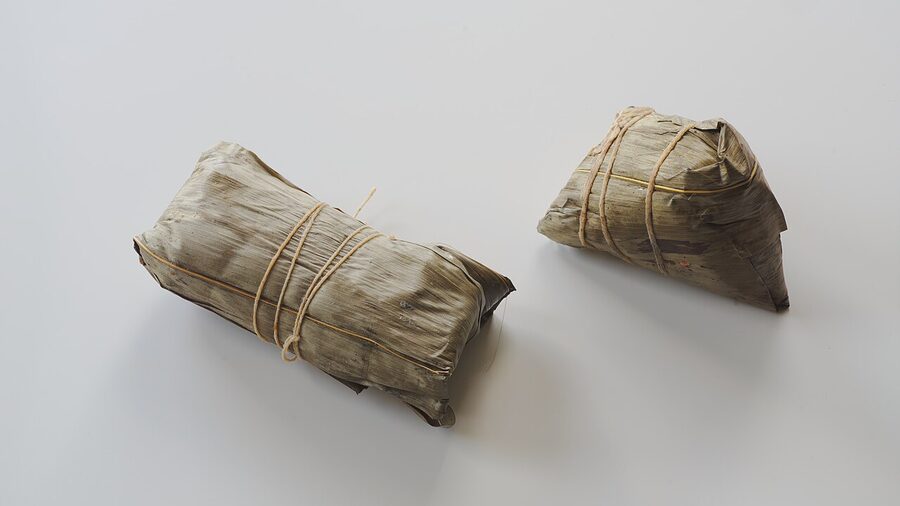 Two zongzi sticky-rice dumplings wrapped in bamboo leaves in different regional styles