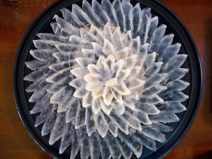 Thin sliced fugu sashimi arranged as a chrysanthemum on a plate