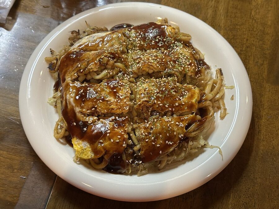 Hiroshima okonomiyaki cooking on a teppan with noodles visible