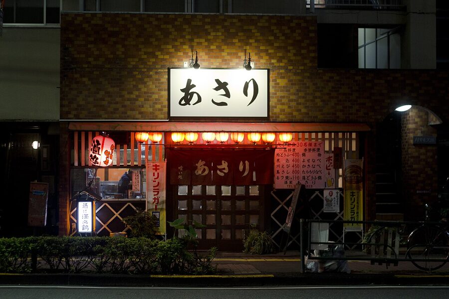 Exterior of a traditional izakaya in Gotanda, Tokyo, with red lanterns and hand-painted menu boards