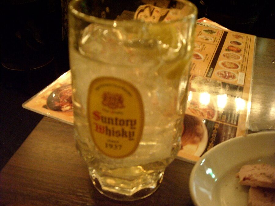 Whisky highball with a lemon slice and ice cubes on a wooden bar top