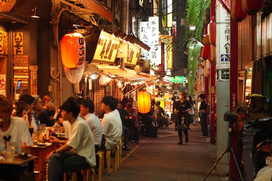 People eating at izakaya alley stalls in Shinjuku, Tokyo, at dusk under paper lanterns