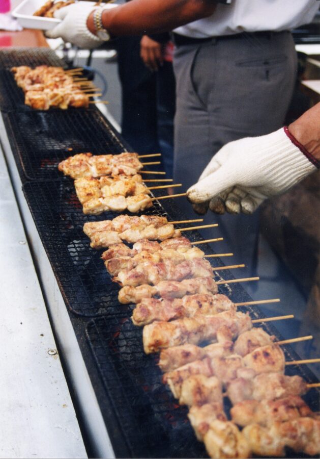 Yakitori chicken skewers grilling over glowing charcoal with smoke rising