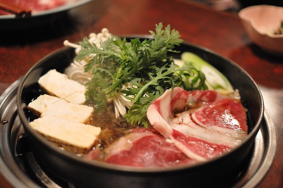 A traditional sukiyaki pot with beef, leek, and tofu cooking in sweet soy broth