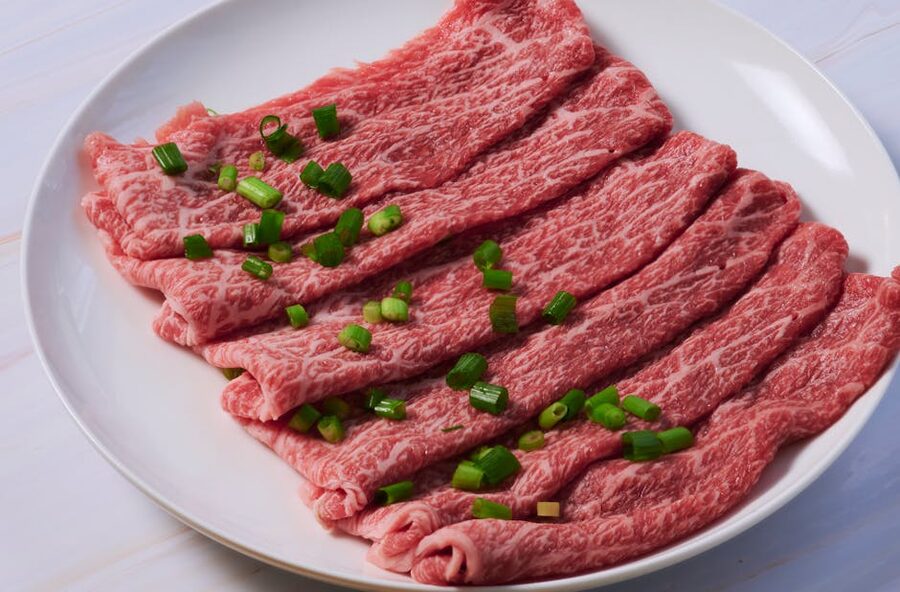 Thinly sliced wagyu beef arranged on a plate with green onion garnish