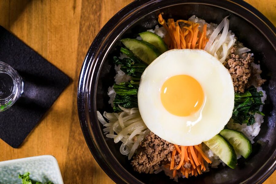 Korean bibimbap in a black ceramic bowl with rice, vegetables and egg