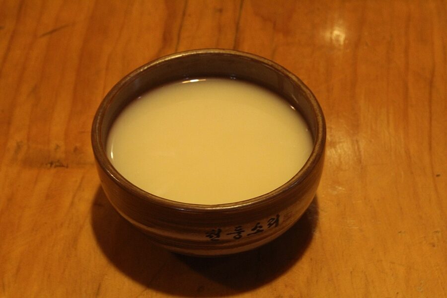 A bowl of cloudy white Korean makgeolli rice wine with a wooden ladle