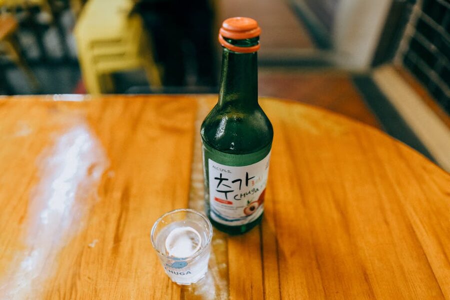 A green bottle of Korean soju with a shot glass on a wooden table
