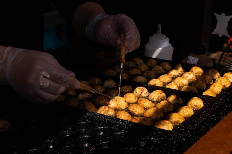 Hands turning takoyaki on a hot griddle Osaka street food