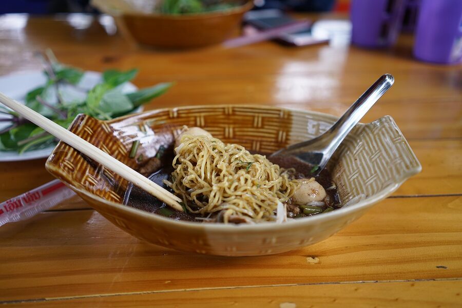 Close-up Thai boat noodle bowl with herbs and broth