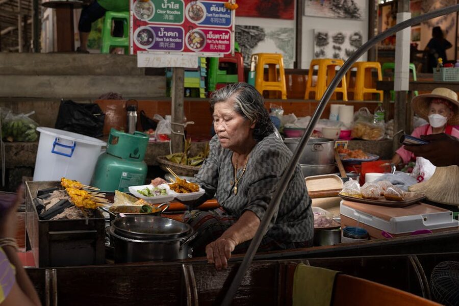 Thai woman cooking at a Bangkok street food stall with steaming noodles