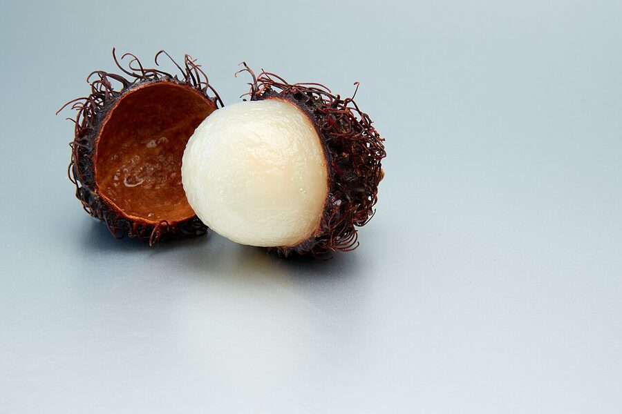 Rambutan half-peeled showing the white flesh inside the red hairy skin